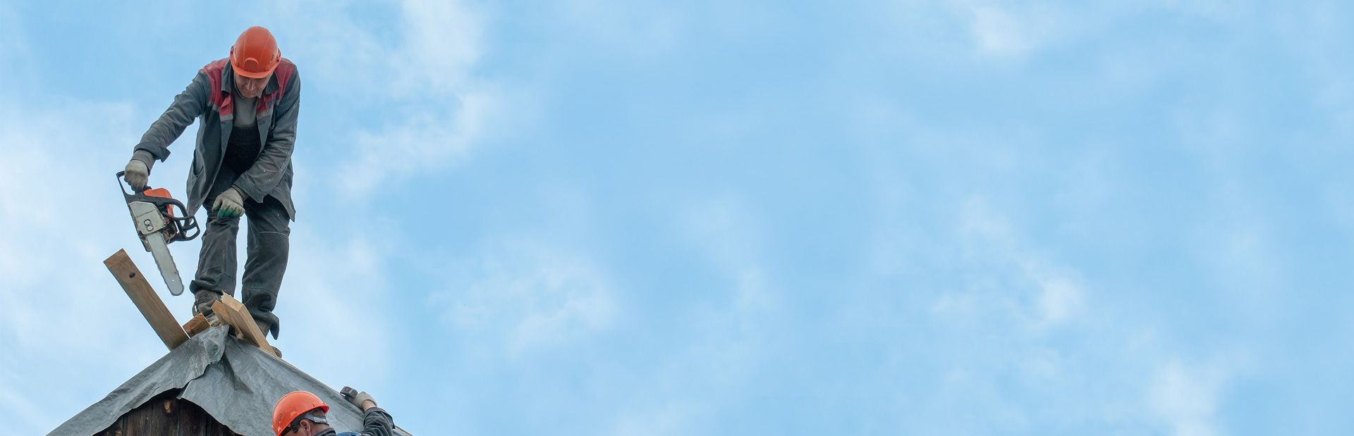Roofer repairing a residential roof against a blue sky